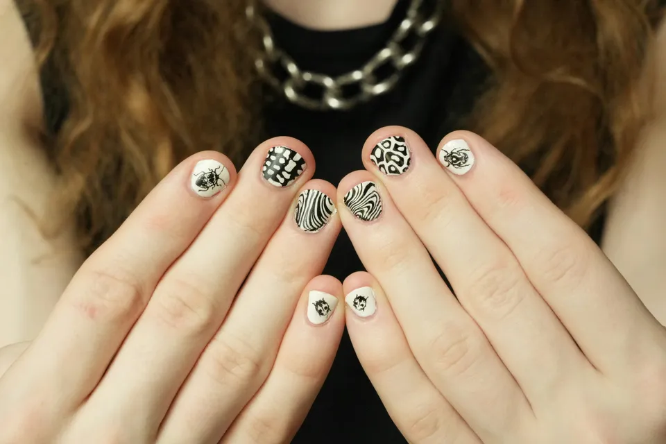 Two hands held up with short white nails hand-painted in black — zebra stripes, leopard spots and small beetles