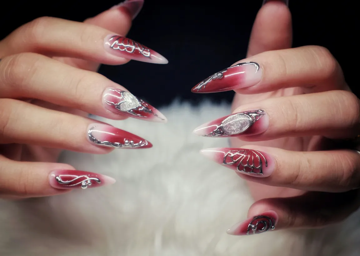 Long stiletto nails in deep red ombré with silver chrome linework, glitter accents and hand-painted detail