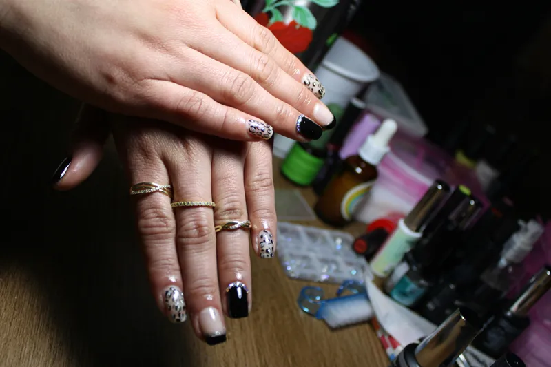 Two hands held over a nail desk of bottles and brushes, nails in cream and black leopard print with rhinestones and glossy black tips